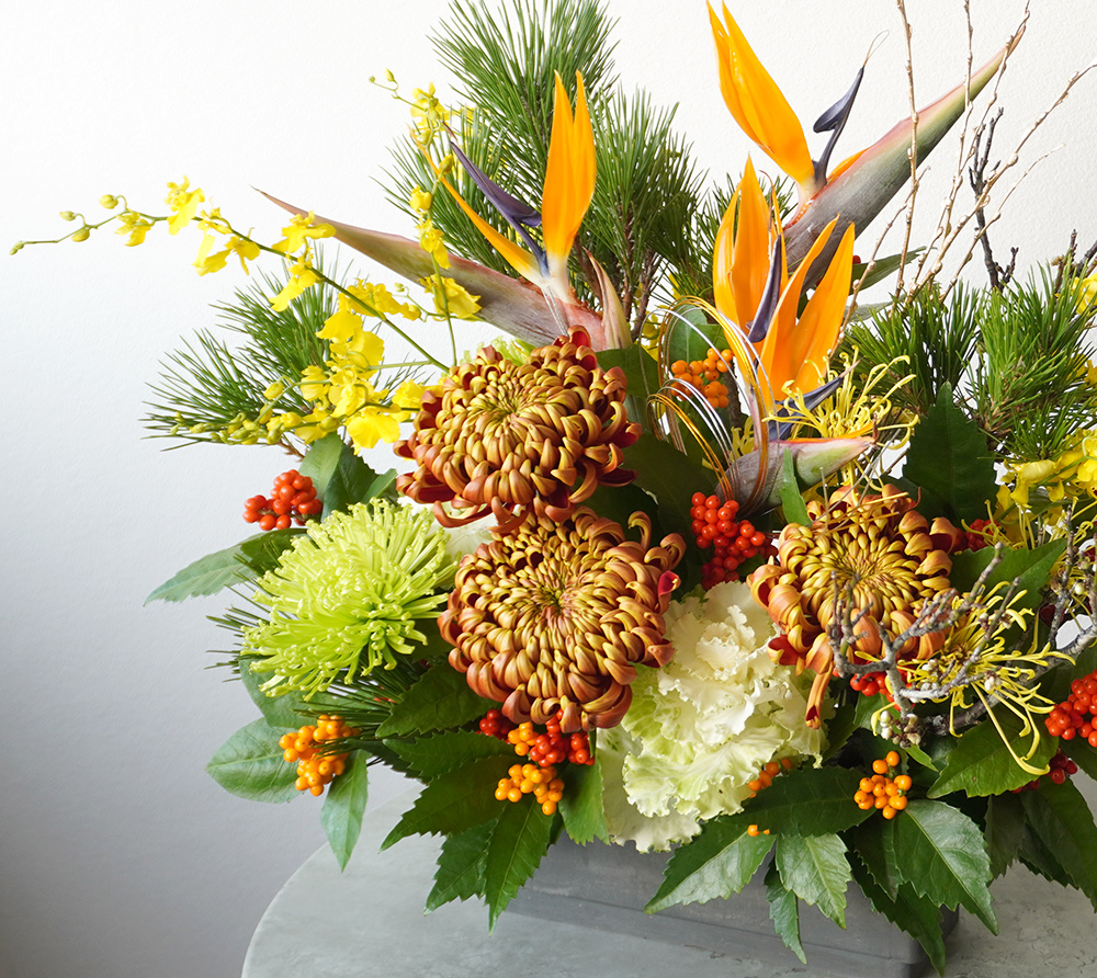 根引松やストレチア、オレンジの複色のマムのアレンジメント